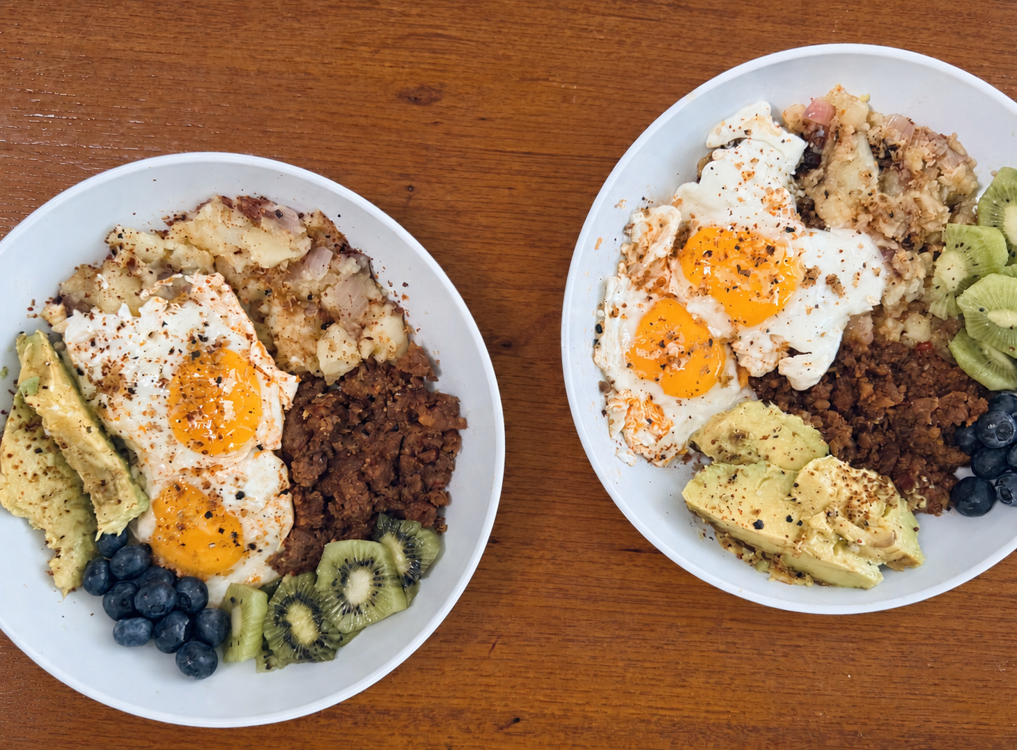 Two generous brunch bowls with eggs, avocado, fruit, and grains