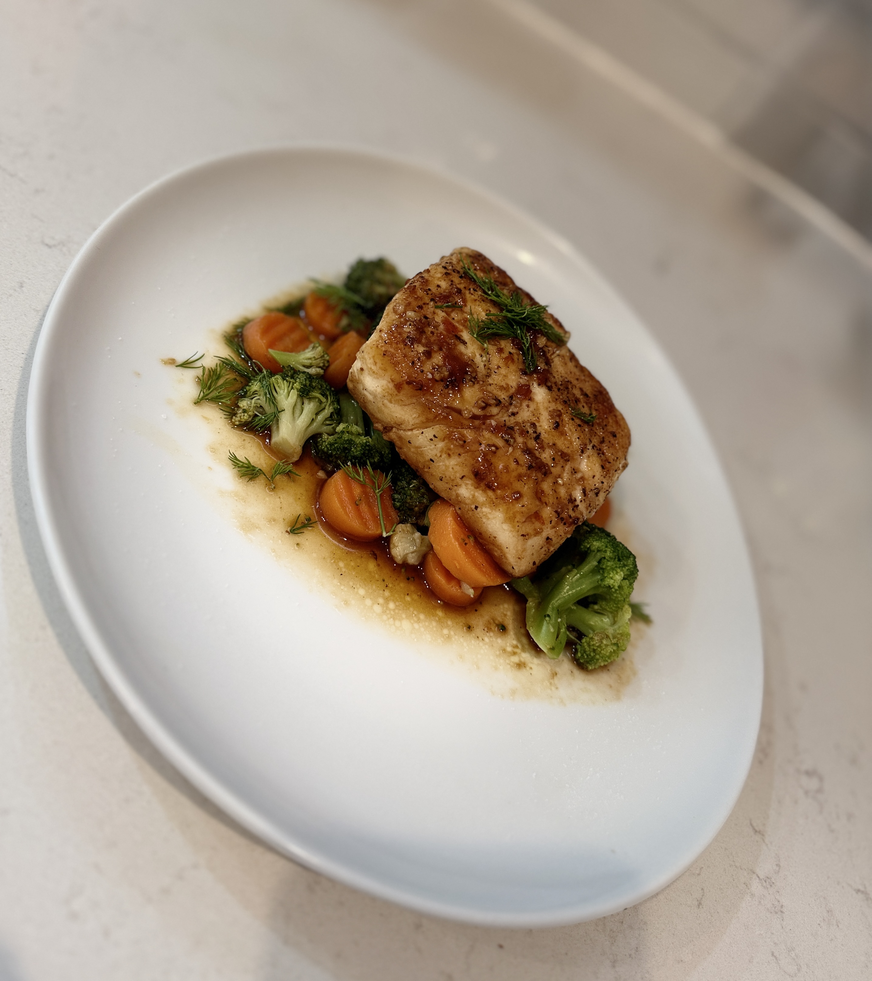 Freshly plated dinner with broccoli, carrots, dill, and pan sauce